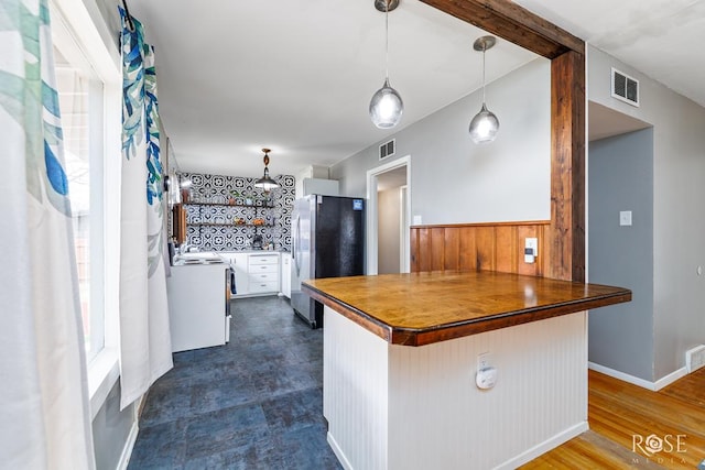 kitchen with a breakfast bar area, a peninsula, visible vents, hanging light fixtures, and freestanding refrigerator