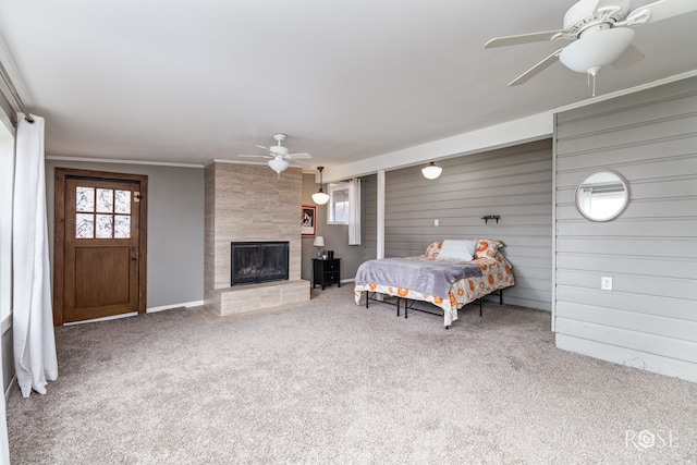 bedroom featuring a tile fireplace, wooden walls, a ceiling fan, carpet, and crown molding