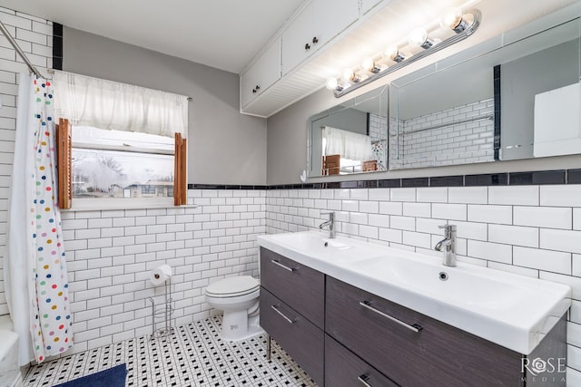 bathroom featuring double vanity, tile walls, toilet, and a sink