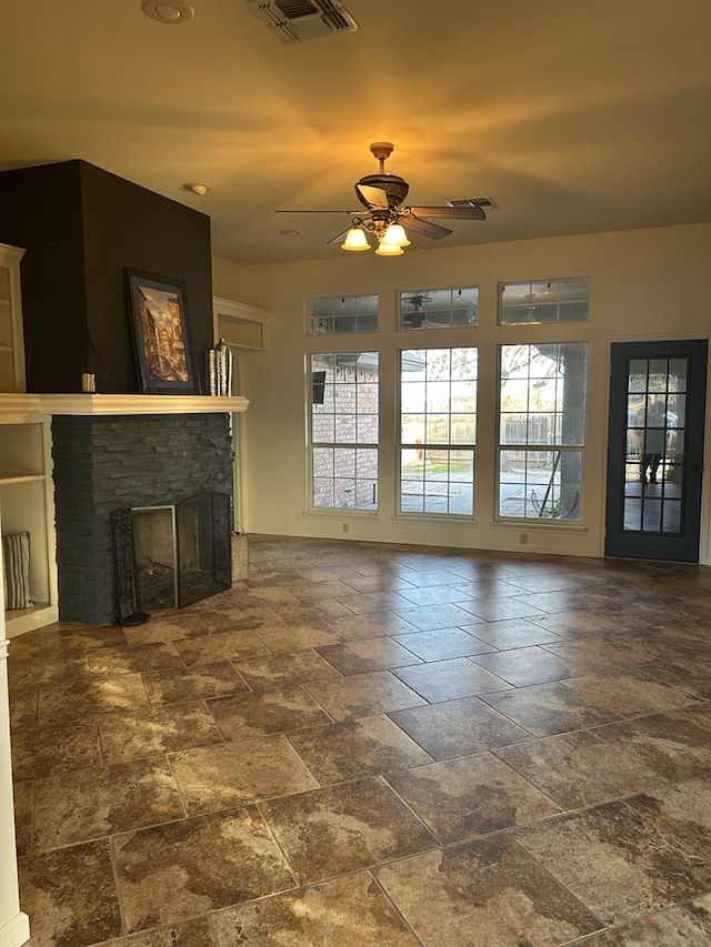 unfurnished living room featuring a stone fireplace and ceiling fan