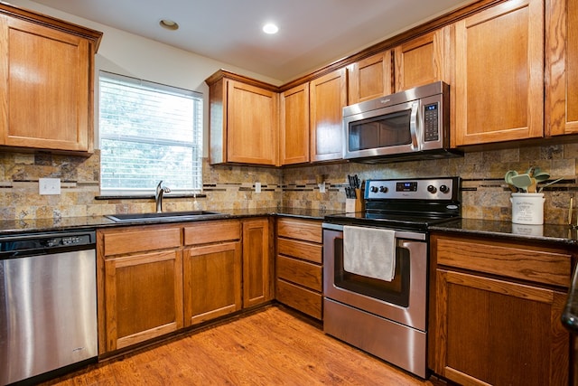 4974 Scarlet Oak Dr, San Angelo, TX 76904 - kitchen featuring appliances with stainless steel finishes, light wood-type flooring, tasteful backsplash, dark stone counters, and brown cabinetry