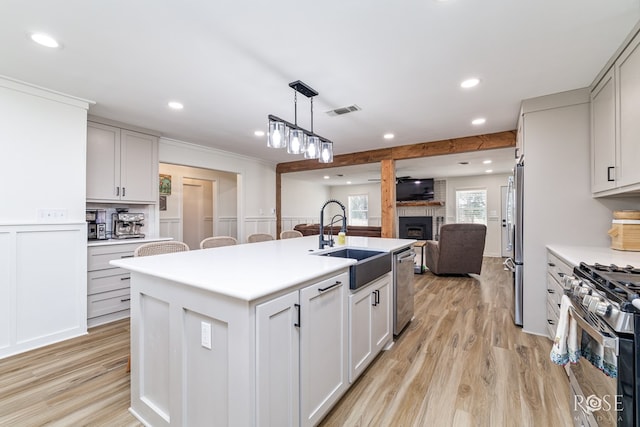 kitchen featuring visible vents, light wood-style flooring, a sink, a brick fireplace, and open floor plan