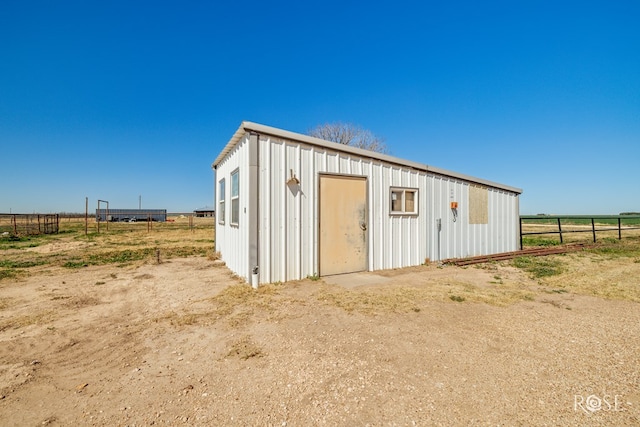 view of outbuilding featuring a rural view, an outdoor structure, and fence