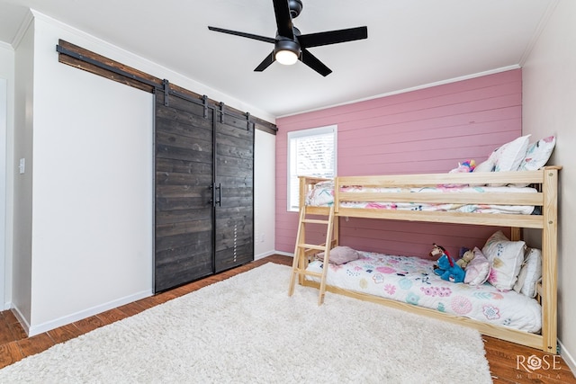 bedroom featuring ornamental molding, wood finished floors, a barn door, baseboards, and ceiling fan