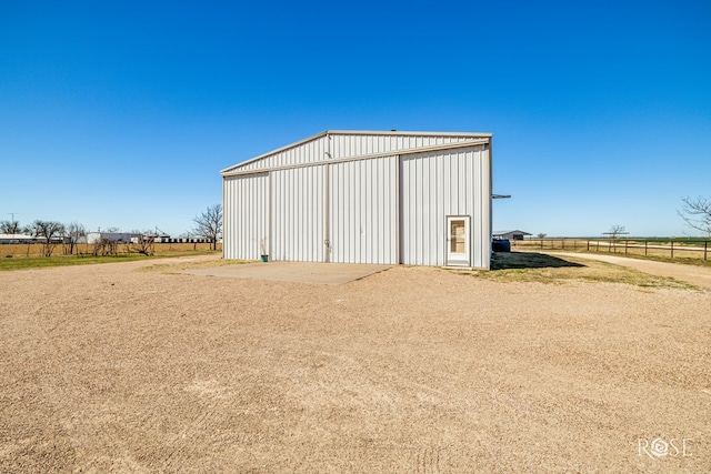 view of pole building featuring a rural view, driveway, and fence