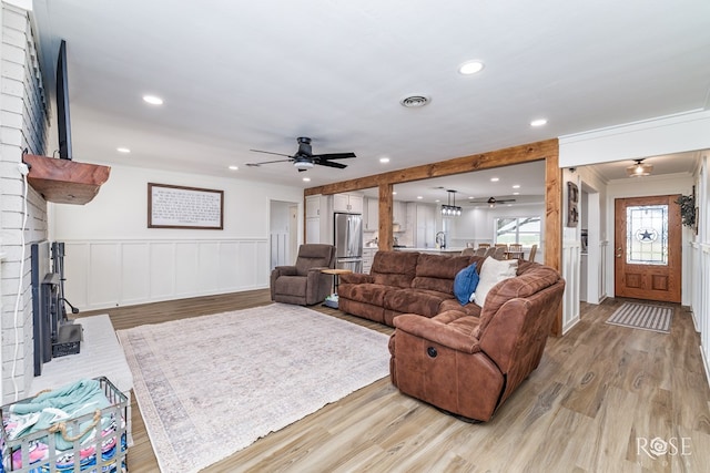 living area with light wood finished floors, visible vents, ceiling fan, a wainscoted wall, and ornamental molding