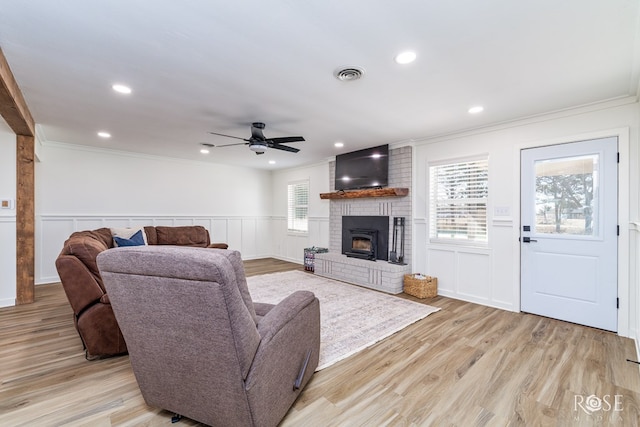 living area featuring a brick fireplace, light wood-style flooring, visible vents, and ornamental molding