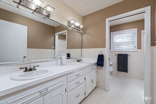 2305 Douglas Dr, San Angelo, TX 76904 - full bath featuring toilet, tile patterned floors, double vanity, wainscoting, and tile walls