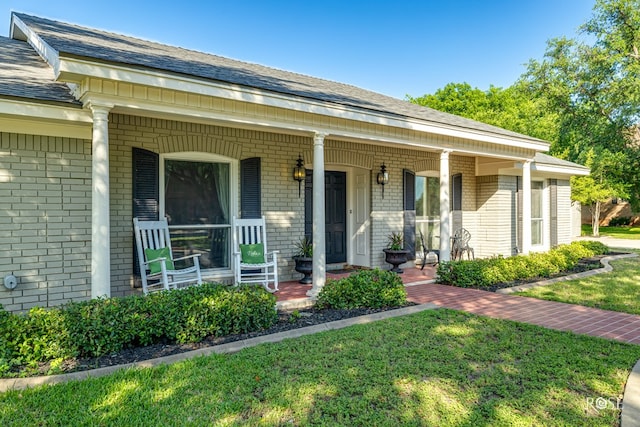 2305 Douglas Dr, San Angelo, TX 76904 - view of exterior entry with brick siding, a porch, a shingled roof, and a yard