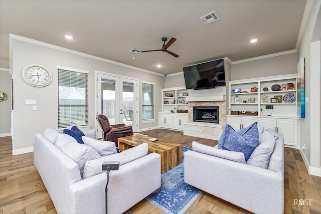 living room with french doors, ornamental molding, a fireplace, and light wood-type flooring