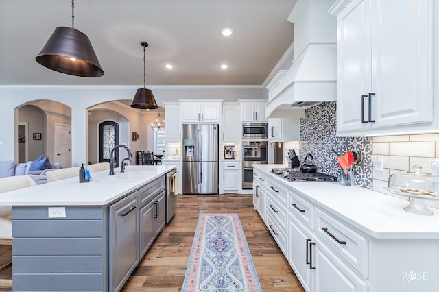 kitchen with stainless steel appliances, an island with sink, pendant lighting, and white cabinetry