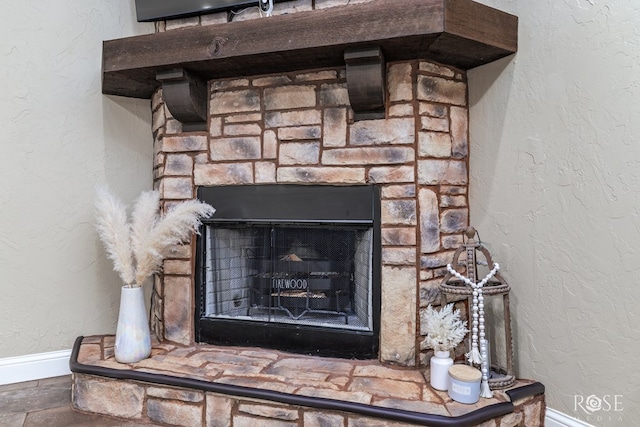 details featuring a textured wall, a stone fireplace, and baseboards