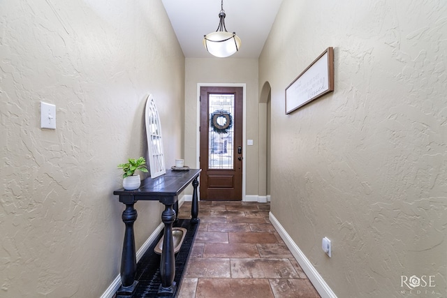 doorway to outside featuring baseboards, arched walkways, and a textured wall