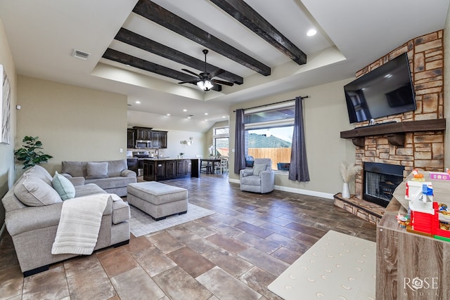 living area with a stone fireplace, a ceiling fan, visible vents, baseboards, and beamed ceiling