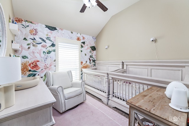 bedroom featuring wallpapered walls, a ceiling fan, wainscoting, lofted ceiling, and a nursery area