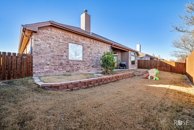 rear view of house with a chimney, brick siding, a patio, and a fenced backyard