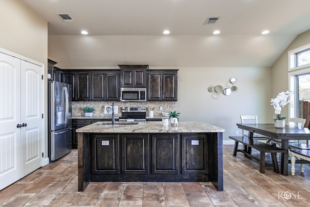 kitchen featuring light stone countertops, a center island with sink, appliances with stainless steel finishes, and decorative backsplash