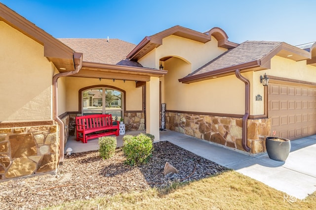 view of exterior entry featuring a garage, stone siding, roof with shingles, and stucco siding