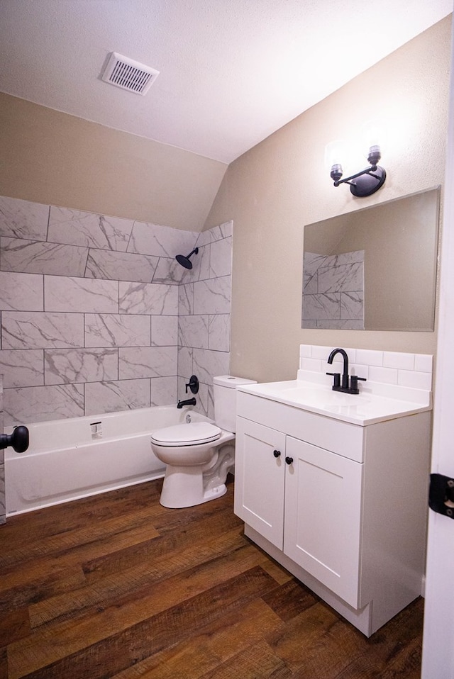 full bathroom featuring vaulted ceiling, hardwood / wood-style flooring, vanity, tiled shower / bath combo, and toilet