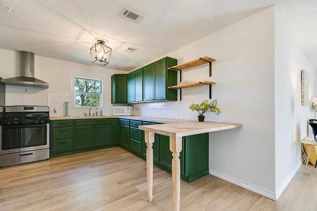 kitchen featuring green cabinetry, wall chimney exhaust hood, light hardwood / wood-style floors, and stainless steel gas stove