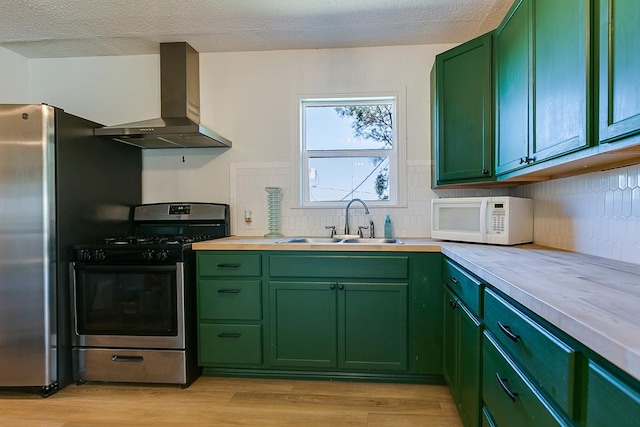 kitchen featuring wall chimney range hood, sink, stainless steel appliances, green cabinetry, and light wood-type flooring