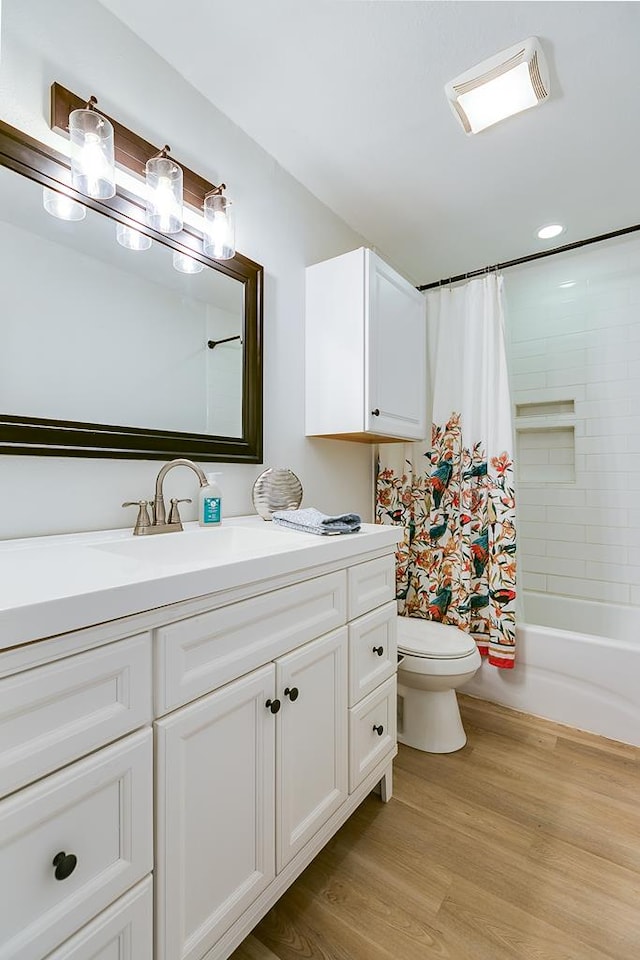 full bathroom featuring wood-type flooring, toilet, shower / bath combo with shower curtain, and vanity