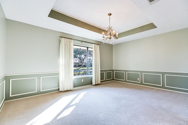 carpeted empty room with a tray ceiling, a chandelier, and a textured ceiling