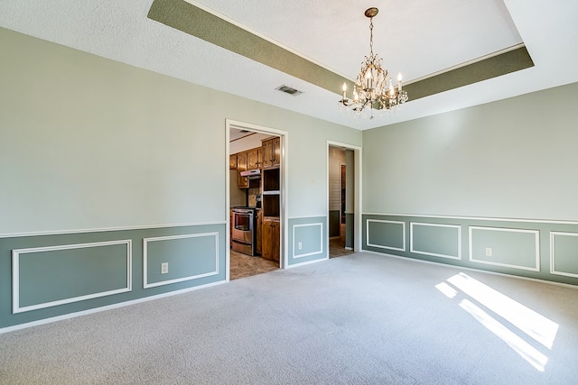 carpeted spare room featuring a tray ceiling, a chandelier, and a textured ceiling