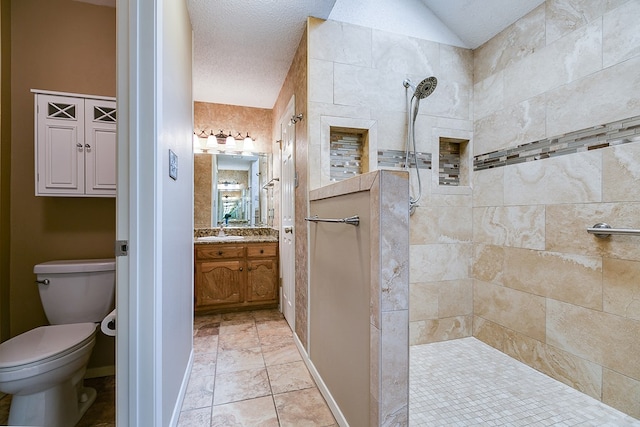 bathroom with a tile shower, lofted ceiling, vanity, toilet, and a textured ceiling