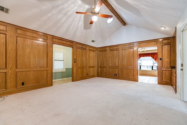 unfurnished bedroom featuring light carpet, a textured ceiling, beam ceiling, and wood walls