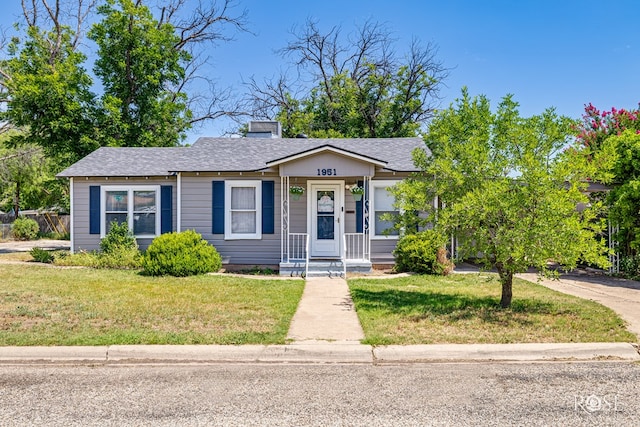 1951 W Twohig Ave, San Angelo, TX 76901 - view of front of house featuring a front lawn, a shingled roof, a porch, and a chimney