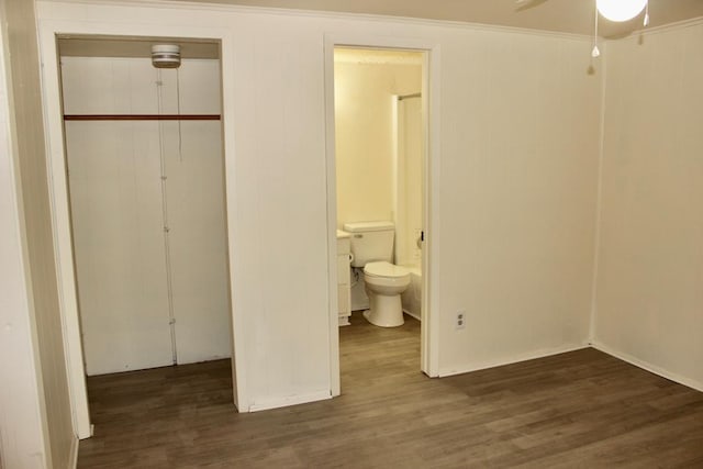 unfurnished bedroom featuring crown molding, ceiling fan, ensuite bathroom, dark hardwood / wood-style flooring, and a closet