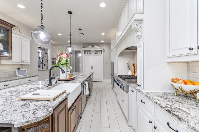 kitchen featuring glass insert cabinets, white cabinetry, hanging light fixtures, and an island with sink