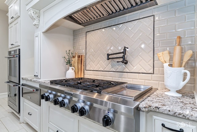 kitchen with a warming drawer, stainless steel appliances, tasteful backsplash, white cabinetry, and light stone countertops