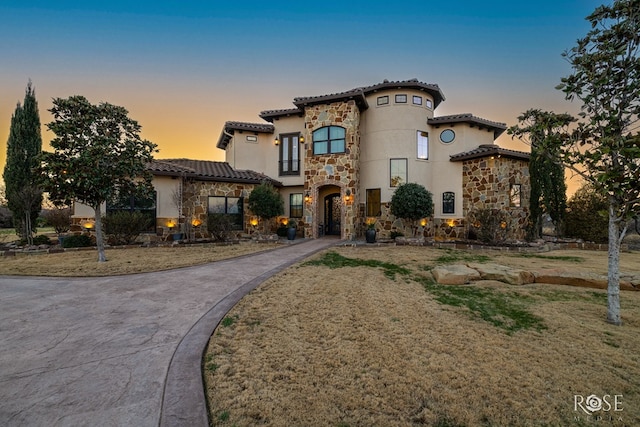 mediterranean / spanish home with stone siding, driveway, a tiled roof, and stucco siding