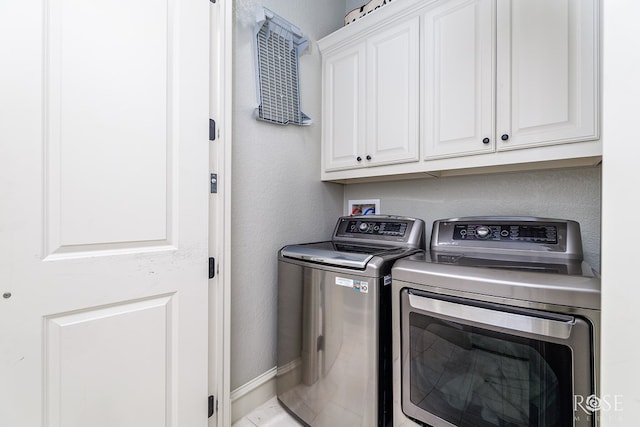 laundry room featuring cabinet space, baseboards, a textured wall, and washing machine and clothes dryer