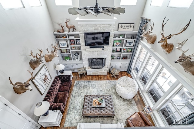 living room featuring ceiling fan, a fireplace with raised hearth, and wood finished floors