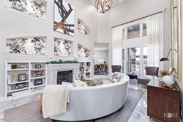 living room featuring a towering ceiling, a fireplace, built in features, and a notable chandelier