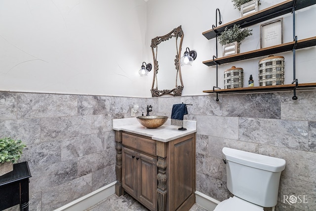 half bath featuring toilet, a wainscoted wall, tile walls, and vanity