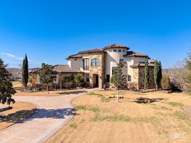 mediterranean / spanish home featuring stone siding, a tiled roof, curved driveway, and stucco siding