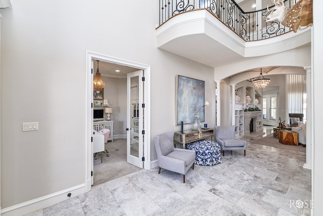 entryway with a fireplace with raised hearth, arched walkways, a high ceiling, baseboards, and ornate columns