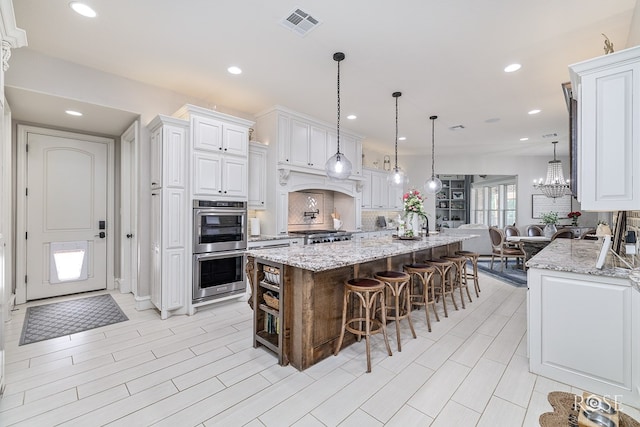 kitchen with white cabinets, a large island, light stone counters, stainless steel double oven, and pendant lighting