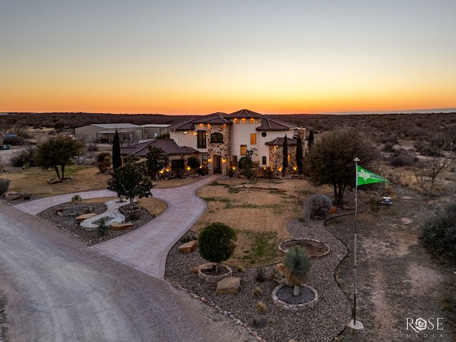 view of front of property featuring stone siding, curved driveway, and stucco siding