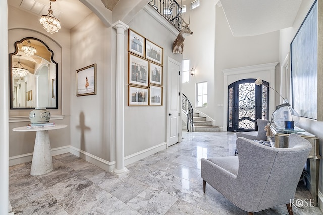 foyer featuring baseboards, arched walkways, a towering ceiling, stairway, and ornate columns