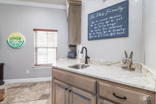 kitchen featuring light stone countertops, a sink, baseboards, ornamental molding, and brown cabinets