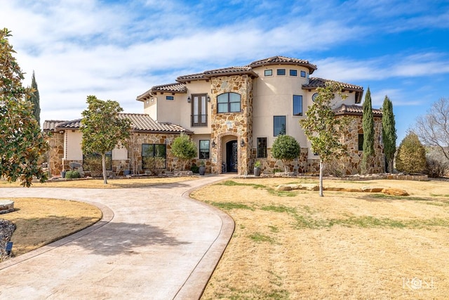 mediterranean / spanish house featuring stone siding, a tile roof, curved driveway, and stucco siding