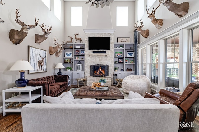 living room with dark wood finished floors, a stone fireplace, a towering ceiling, and ceiling fan