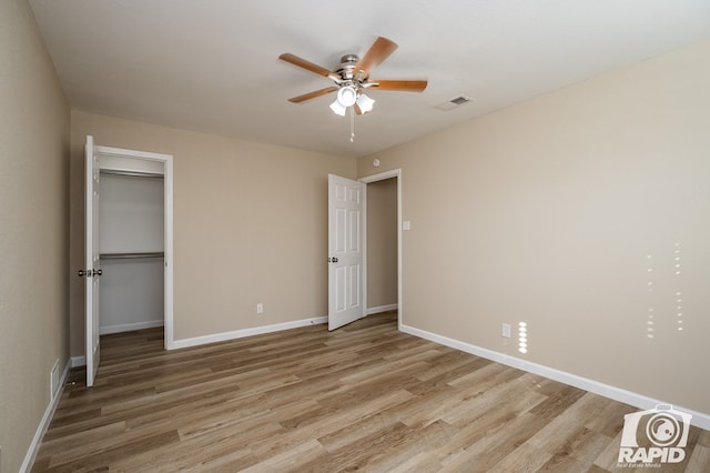 unfurnished bedroom featuring ceiling fan, a spacious closet, and light wood-type flooring