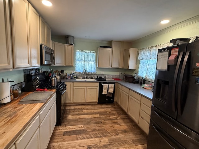 kitchen with ornamental molding, dark wood-type flooring, black appliances, wooden counters, and a sink