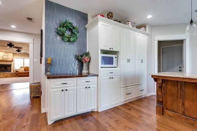 kitchen with white microwave, visible vents, wood finished floors, and a stone fireplace